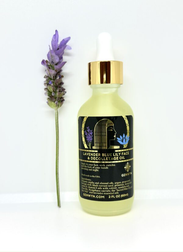 A bottle of lavender blue body oil next to a purple flower.