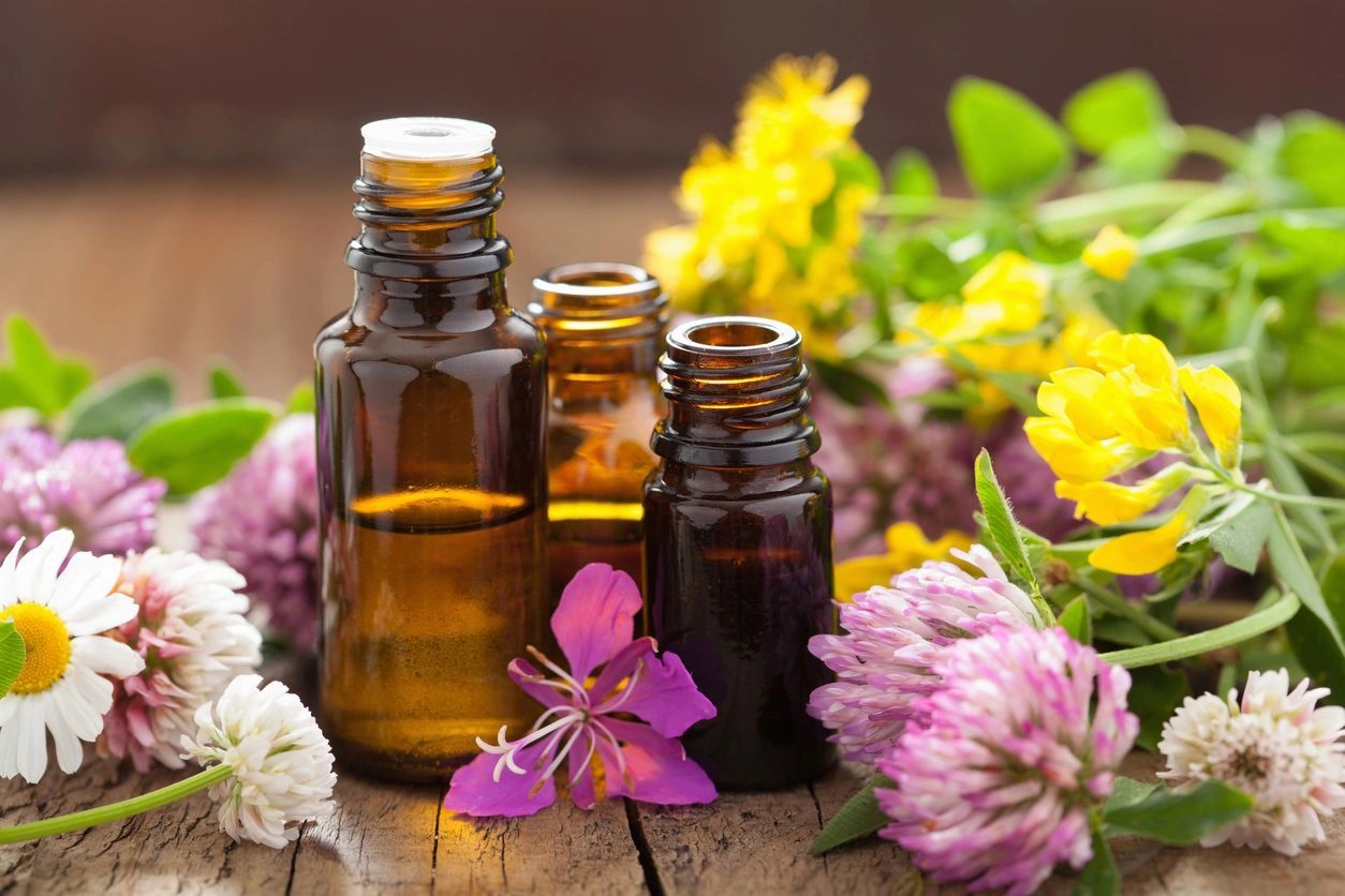 Three bottles of essential oils and flowers on a table.